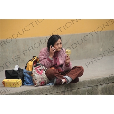 Woman Spinning a Prayer Wheel and Talking on a Mobile Phone beside West Lake (Xihu) in Hangzhou